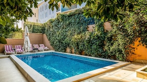 Ein rechteckiger Pool mit gefliestem Sonnendeck, umgeben von Liegestühlen und einer überdachten Sitzgruppe.