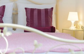 A neatly made bed with pink bedding and a white headboard. There is a bedside table with a lamp and a small decorative item. - Apartment Luka - Three Bedroom Apartment (Dubrovnik)