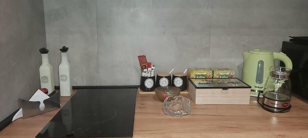 Una cocina con un fogón de inducción negro, dos botellas blancas, una cafetera, un hervidor y una caja de té.