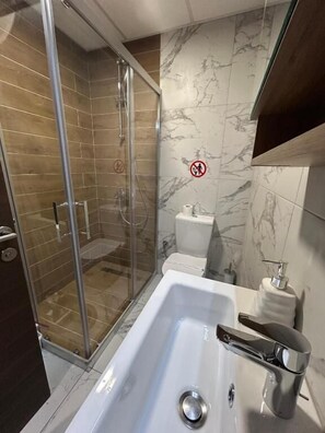 A modern bathroom with a glass-enclosed shower, a white bathtub, and marble walls. - Cozy Skopje Apartment Modern Comforts Scenic Views (Skopje)