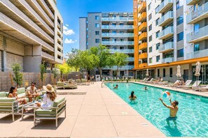 Ein Poolbereich mit Liegestühlen, einem Schwimmbecken und modernen Gebäuden im Hintergrund.