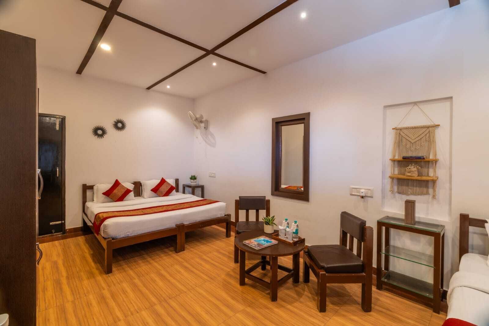 Habitación de hotel con cama, una mesita con sillas, un espejo y una estantería con objetos decorativos.