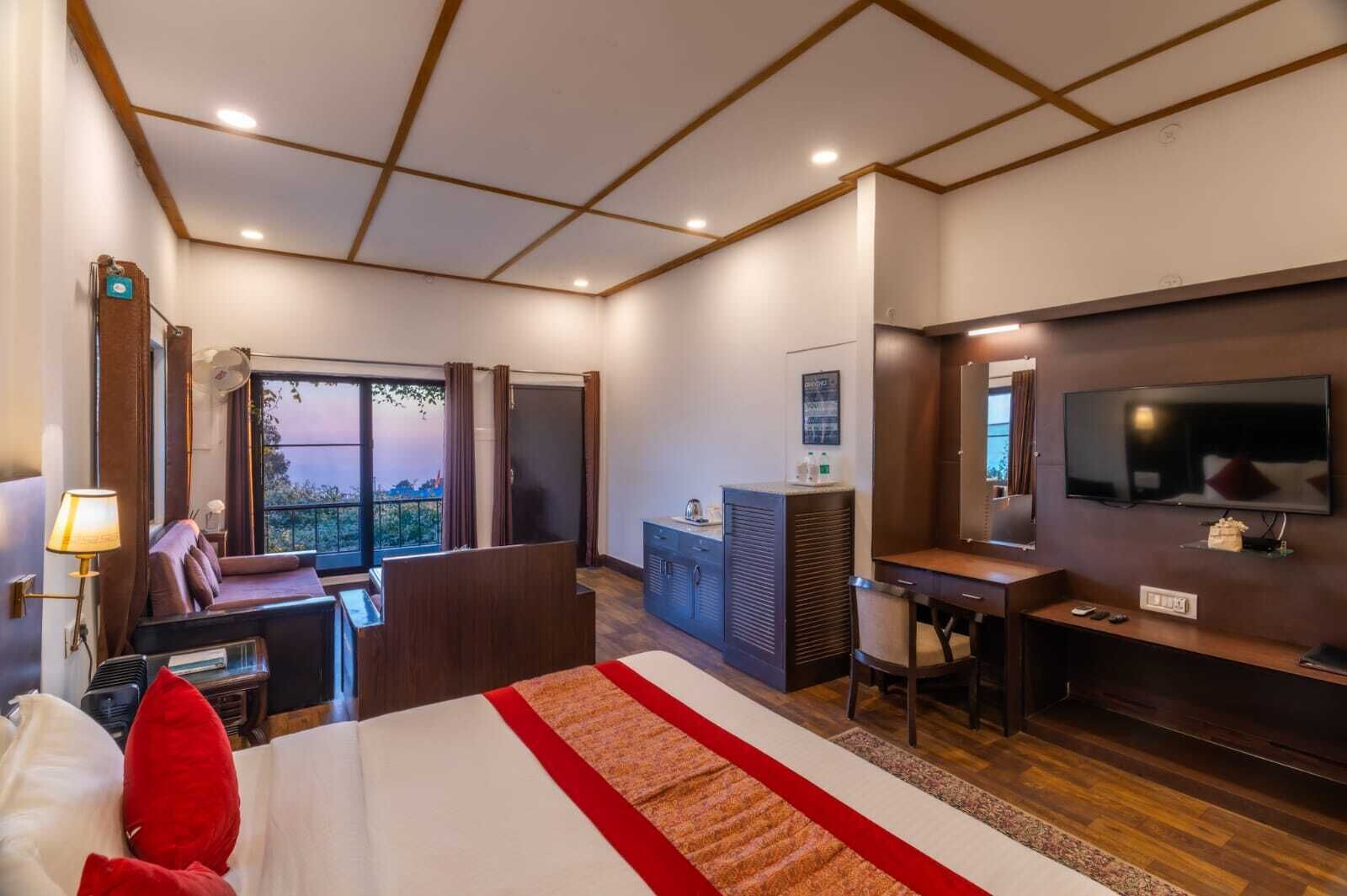 A hotel room with a bed, a desk, a TV, a balcony with curtains, and a city view.