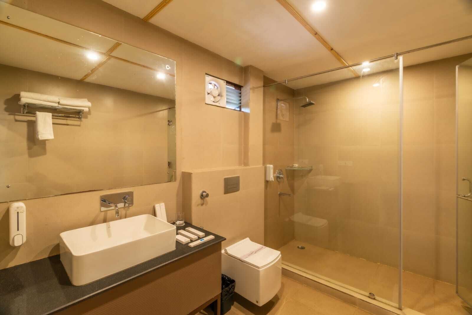 A modern bathroom with a large mirror, a sink, a toilet, and a glass-enclosed shower.