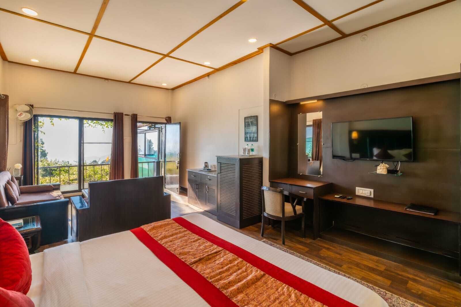 A modern hotel room with a large bed, a desk, a television, and a balcony with a view.