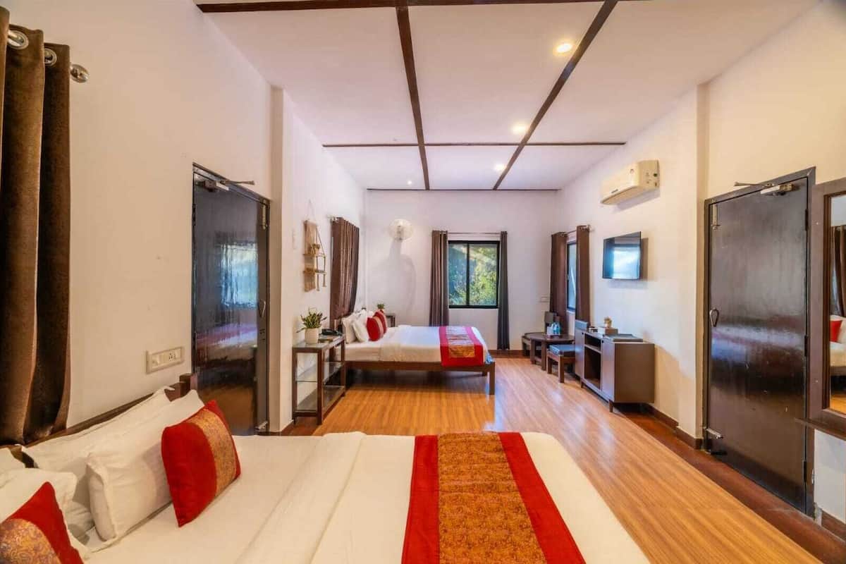 A hotel room with a large bed, a desk, a TV, and a window with a view of greenery.
