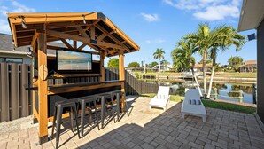 Un patio al aire libre con una pérgola de madera, una parrilla y vistas a la piscina.