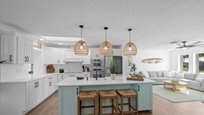 Una cocina moderna con armarios blancos, una isla central con taburetes y lámparas colgantes.