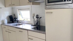 A kitchen with white cabinets, a stainless steel microwave, and a window above the sink. - Minicamping De Lindenhoeve - Chalet Alpaca (Nistelrode)