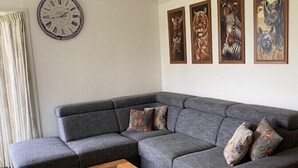 A modern living room with a grey sectional sofa, a wooden coffee table, and four animal-themed paintings on the wall. - Minicamping De Lindenhoeve - Chalet Alpaca (Nistelrode)