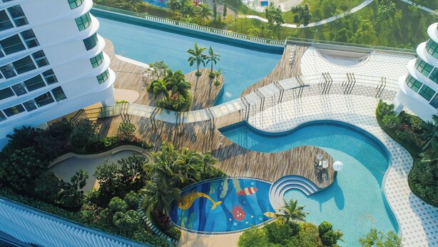 An aerial view of a resort with a large swimming pool, a wooden deck, and lush greenery. - Macrolink Medini Legoland by Stayrene (Iskandar Puteri)