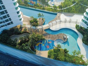 An aerial view of a resort with a large swimming pool, a wooden deck, and lush greenery. - Macrolink Medini Legoland by Stayrene (Iskandar Puteri)