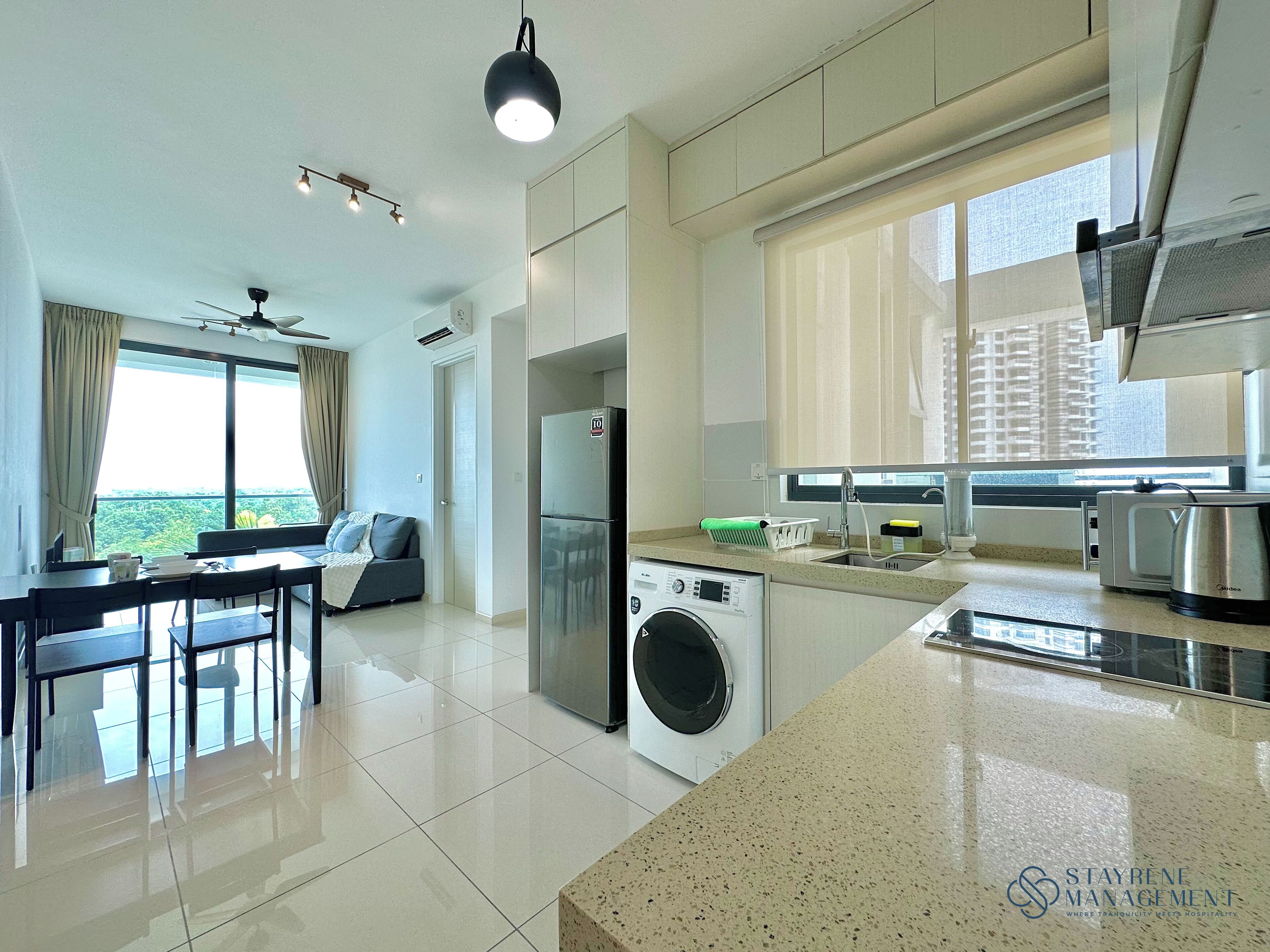 A modern kitchen with a washing machine, a dining area with a table and chairs, and a large window with a view of greenery.