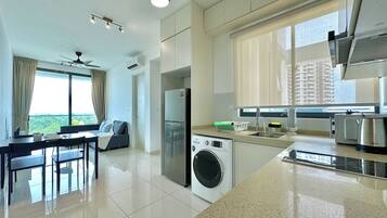 A modern kitchen with a washing machine, a dining area with a table and chairs, and a large window with a view of greenery.
