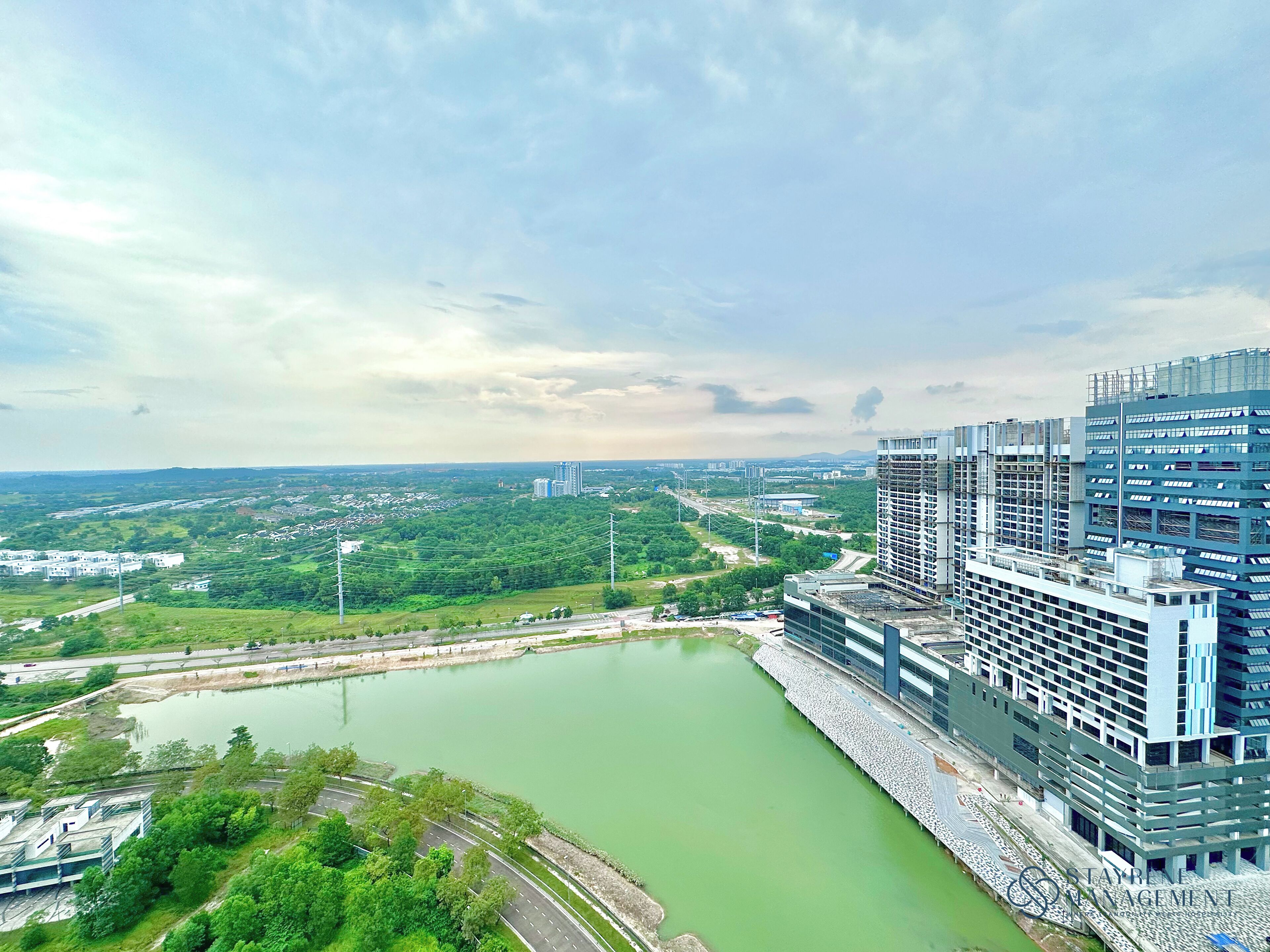 A modern building with a green river in front, surrounded by greenery and other buildings.