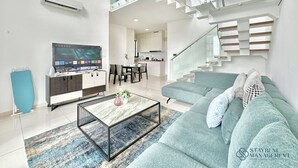 A modern living room with a sofa, a coffee table, and a TV. There's a staircase leading to an upper level. - Macrolink Medini Legoland by Stayrene (Iskandar Puteri)