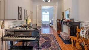 Un vaste hall d’entrée avec un magnifique piano à queue, un tapis à motifs et une cheminée agrémentée de décorations en bois.