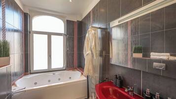 A modern bathroom with a large bathtub, a red sink, and a window providing natural light.