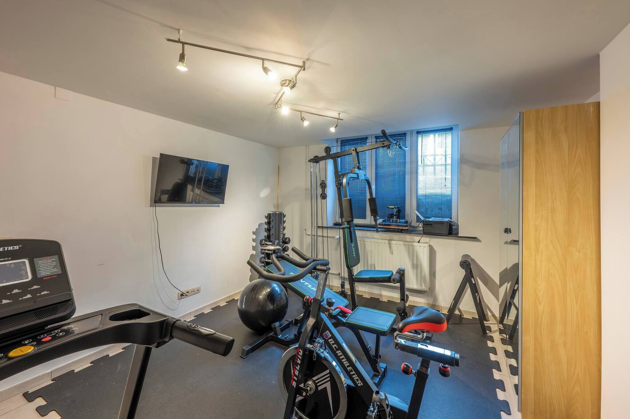 Een fitnessruimte met een loopband, elliptische trainer en gewichtbank.