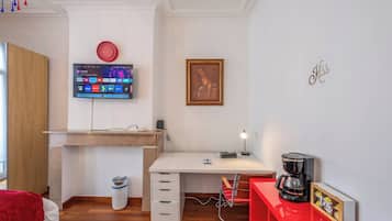 Een moderne kamer met een bureau, een wandtelevisie, een lijst met een afbeelding en een rode koffiezetapparaat.