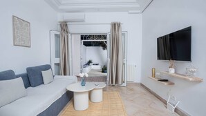 A modern living room with a sofa, two side tables, a TV, and a view into the adjacent room. - Le Petit Zéphyr – House near the beach (La Marsa)