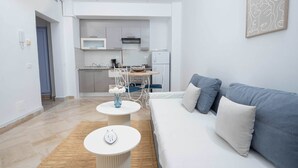 A modern living room with a sofa, a small round table, and a kitchen in the background. - Le Petit Zéphyr – House near the beach (La Marsa)