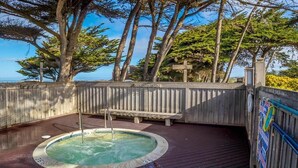 En træterrasse med jacuzzi, omgivet af træer og udsigt til havet.