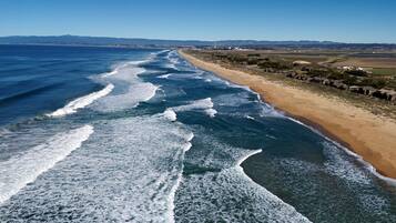 A coastal beach with waves crashing onto the shore, a clear sky, and distant mountains.