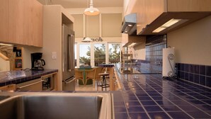 A modern kitchen with a central island, wooden cabinets, and a blue-tiled backsplash. - Monterey Dunes 208 - Moss Landing Townhome - A Mile of Beachfront! (Moss Landing)