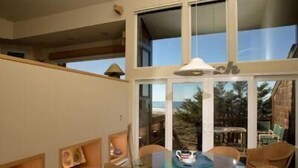 A spacious balcony with a glass table and chairs, overlooking a beach and palm trees. - Monterey Dunes 208 - Moss Landing Townhome - A Mile of Beachfront! (Moss Landing)
