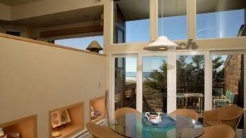 A spacious balcony with a glass table and chairs, overlooking a beach and palm trees.
