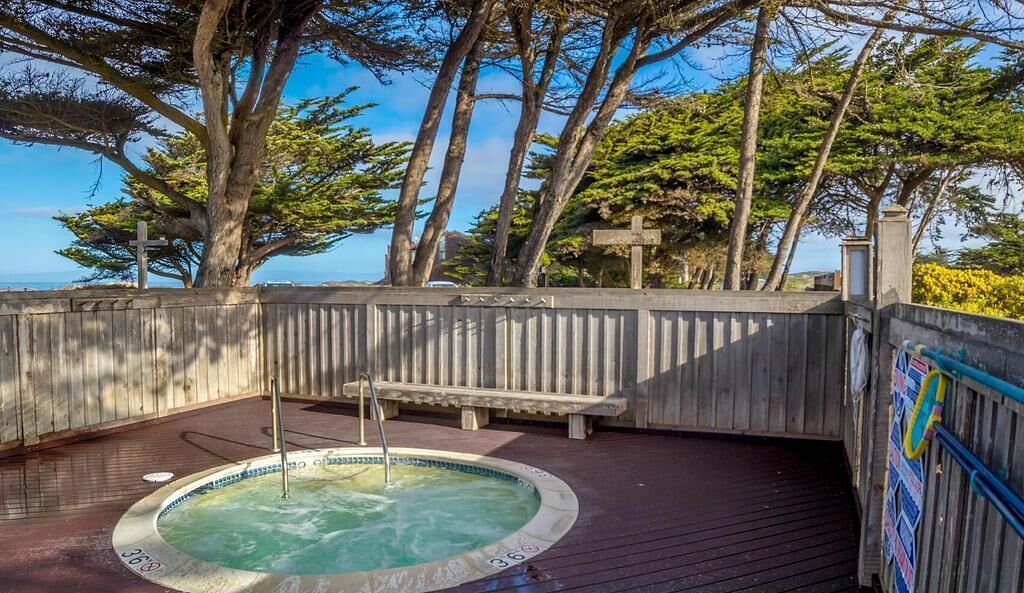 A wooden deck with a hot tub, surrounded by trees and a view of the ocean.