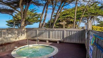 A wooden deck with a hot tub, surrounded by trees and a view of the ocean.
