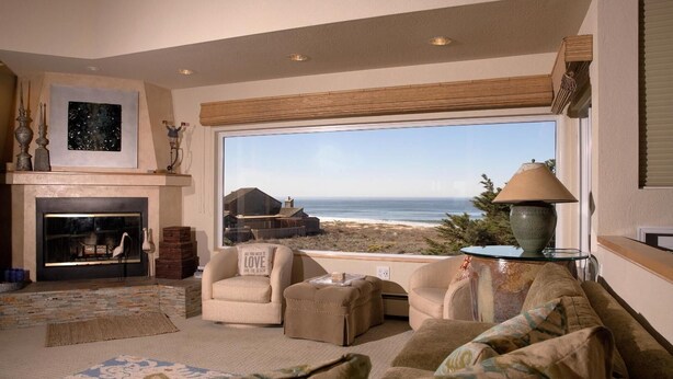 A living room with a fireplace, comfortable seating, and a large window overlooking the beach. - Monterey Dunes 208 - Moss Landing Townhome - A Mile of Beachfront! (Moss Landing)
