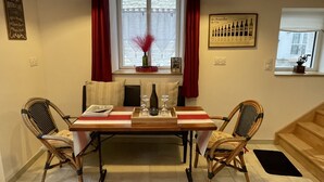 Uma área de refeições com uma mesa posta para dois, com cadeiras de vime, mesa de madeira e um jogo americano vermelho.