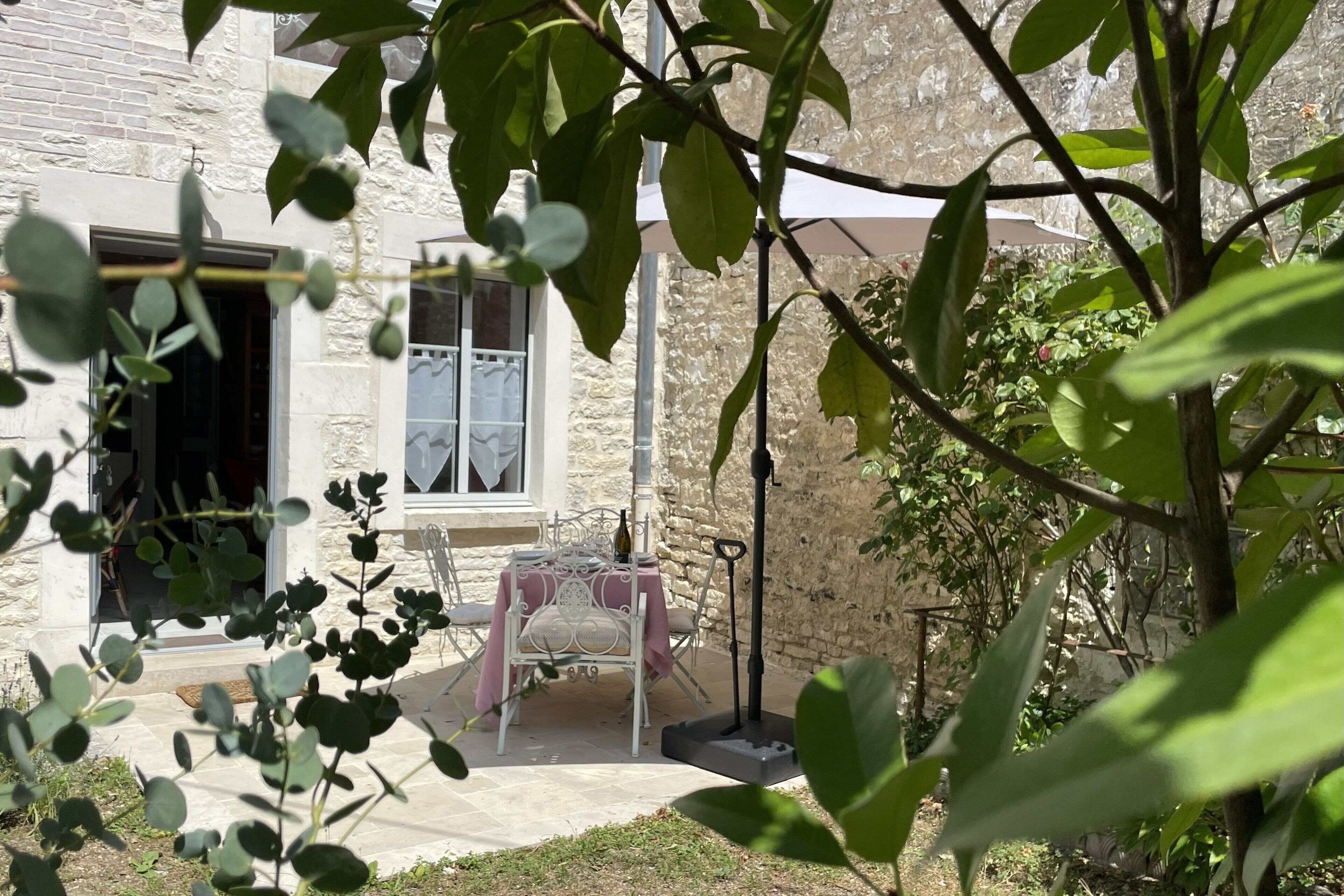 A stone building with a patio area featuring a table and chairs, a bottle, and a metal chair.
