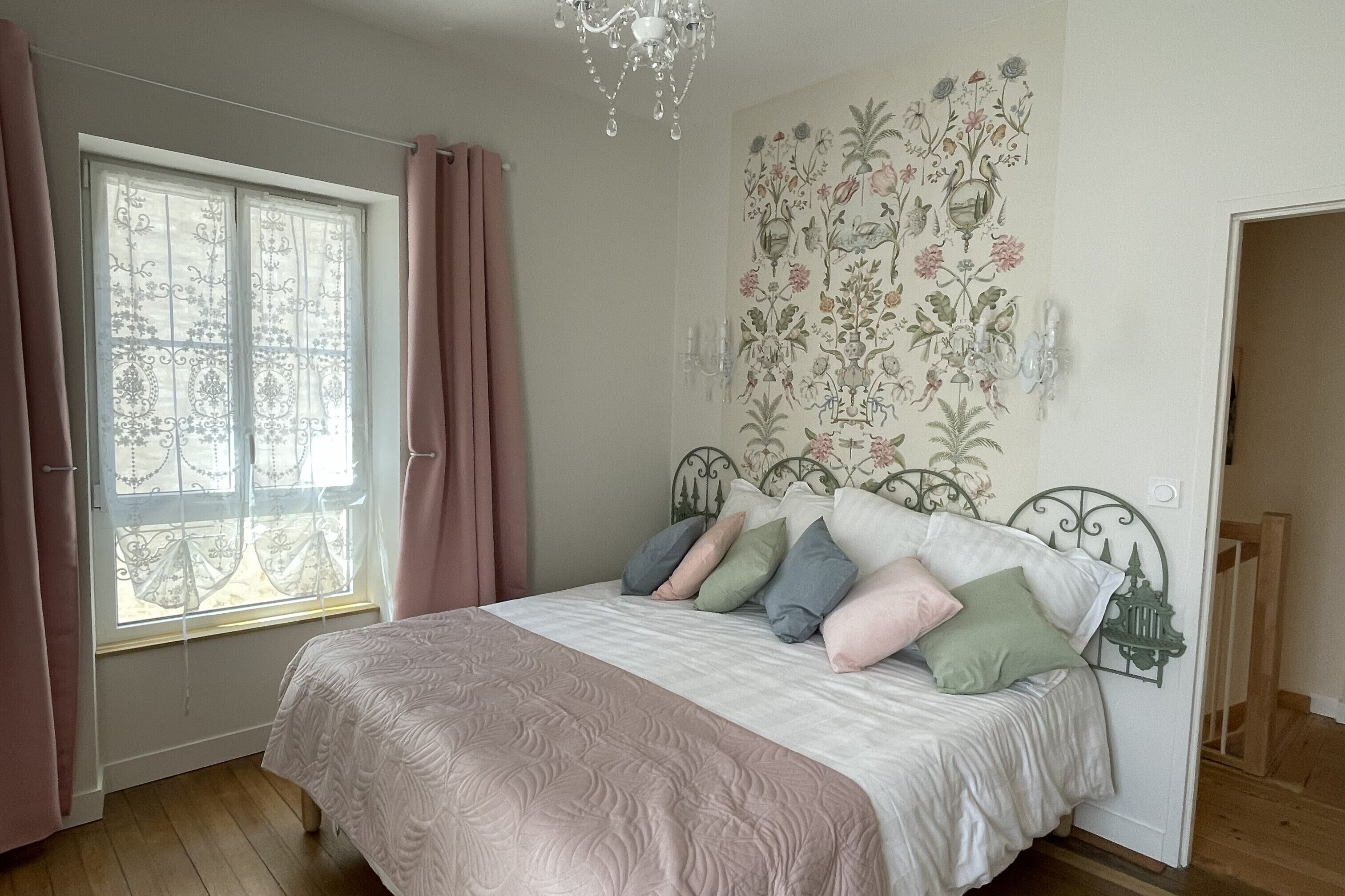 A bedroom with a bed, curtains, a chandelier, and a floral wall mural.
