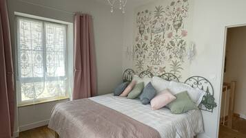 A bedroom with a bed, curtains, a chandelier, and a floral wall mural.