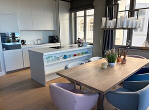 A modern kitchen with white cabinets, a wooden dining table, and blue chairs. - Bluepearl Luxury Apartment, First Row | Ocean View | Terrace | Private Sauna | Fireplace (Binz)