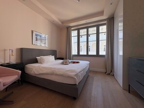 Habitación de hotel con una cama grande, una mesita de noche, una silla, un escritorio y una ventana con cortinas.