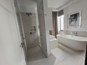 Ein modernes Badezimmer mit bodenebener Dusche, freistehender Badewanne und einem großen Spiegel über dem Waschbecken.