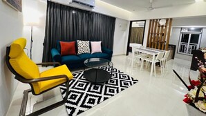 A modern living room with a sofa, a yellow armchair, a coffee table, and a dining area with a table and chairs. - 2BR Service Apartment 302 Chembur by FLORA STAYS (Mumbai)