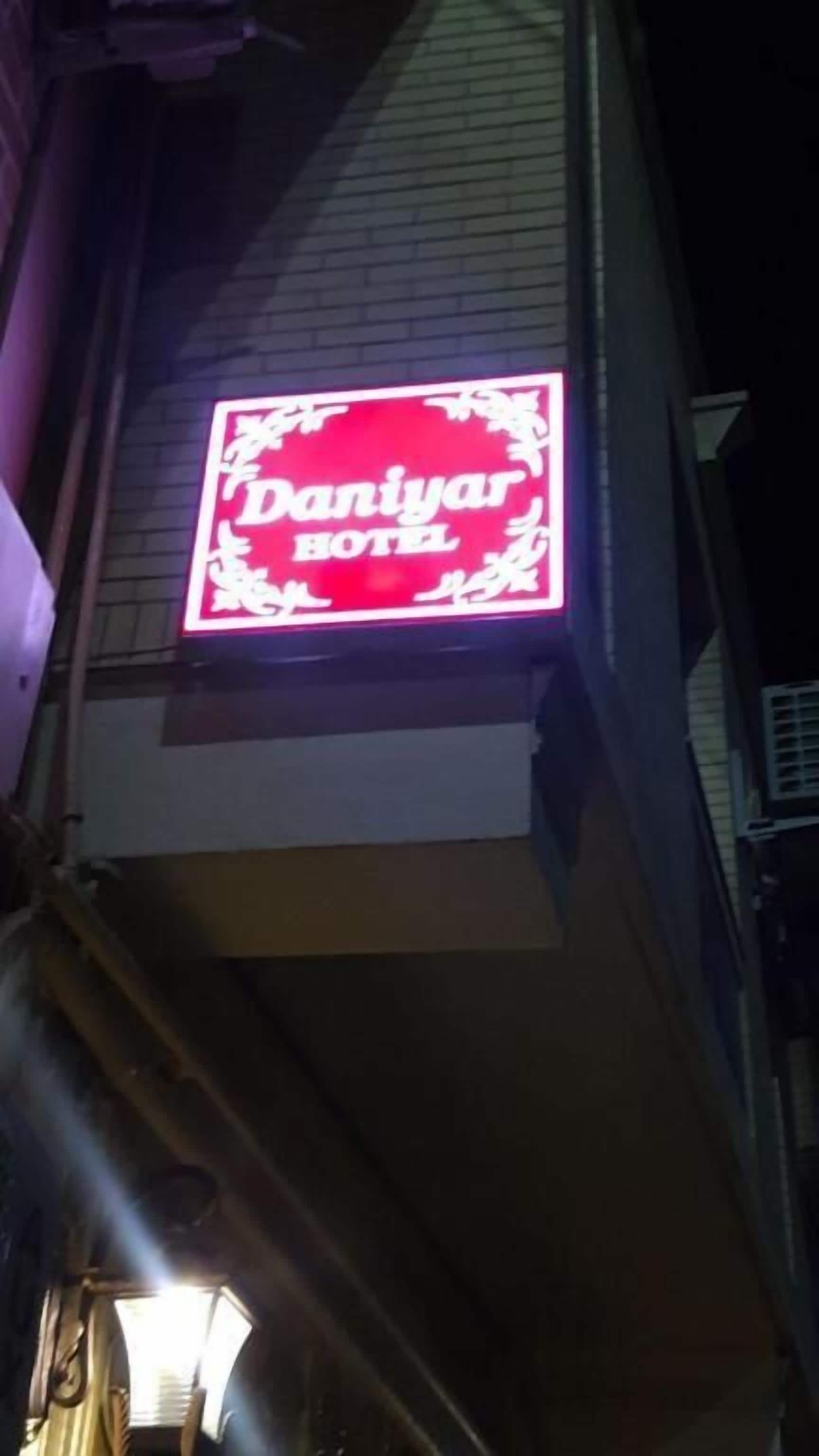 Placa de hotel com o nome 'Daniyar Hotel' em texto branco sobre fundo vermelho.