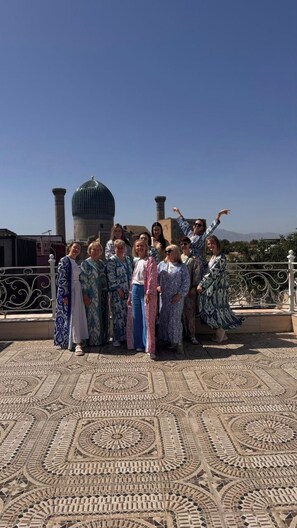 A group of people on a rooftop terrace with a patterned floor and a dome structure in the background. - Daniyar Guest House  (Samarkand)