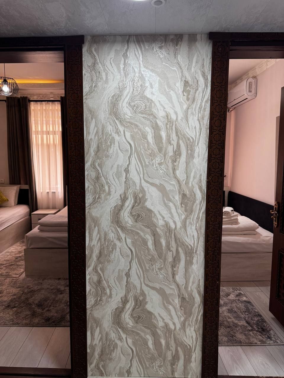 A room with a marble-patterned wall, a bed, a sofa, and a patterned rug.