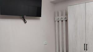 A room with a mounted TV, a small cabinet with drawers, and a wardrobe with a mirror.