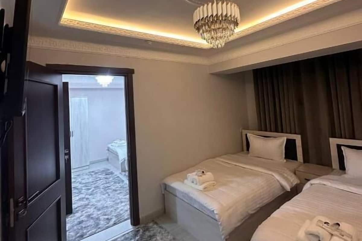 A hotel room with two beds, a chandelier, a door leading to a balcony, and a marble-patterned rug.