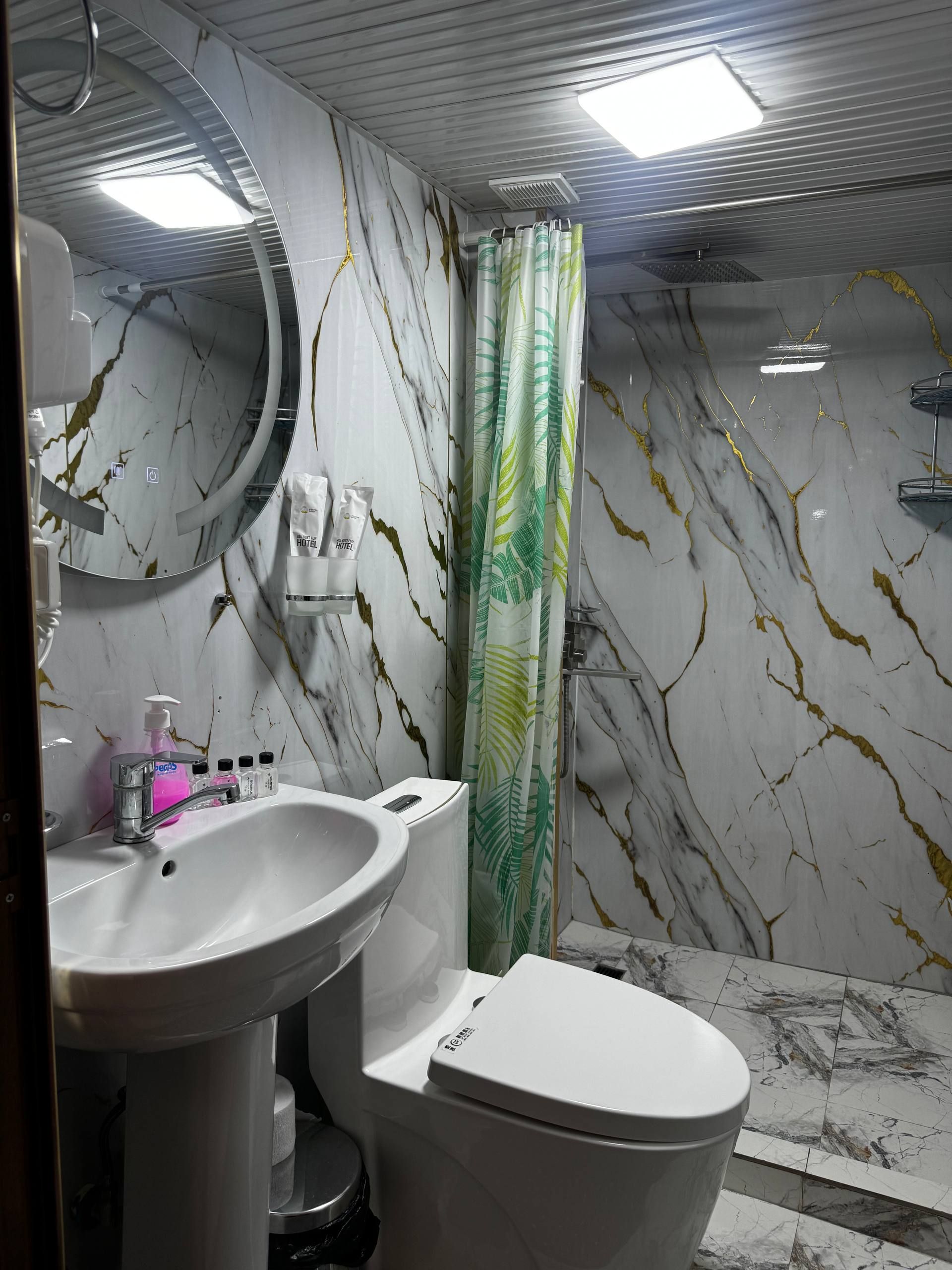A bathroom with a marble wall, a sink, a toilet, a shower curtain, and a mirror.