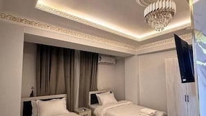 A hotel room with two beds, a chandelier, a wardrobe, and an air conditioning unit.