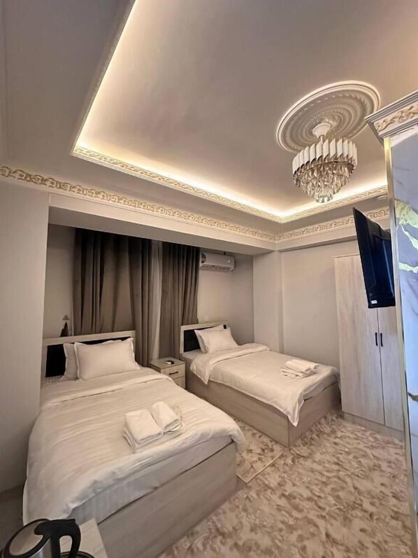 A hotel room with two beds, a chandelier, a wardrobe, and an air conditioning unit. - Daniyar Guest House  (Samarkand)